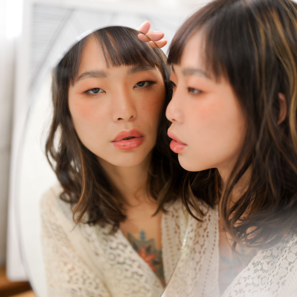 Side view of girl holding up a mirror on the right, with the reflection looking into the camera