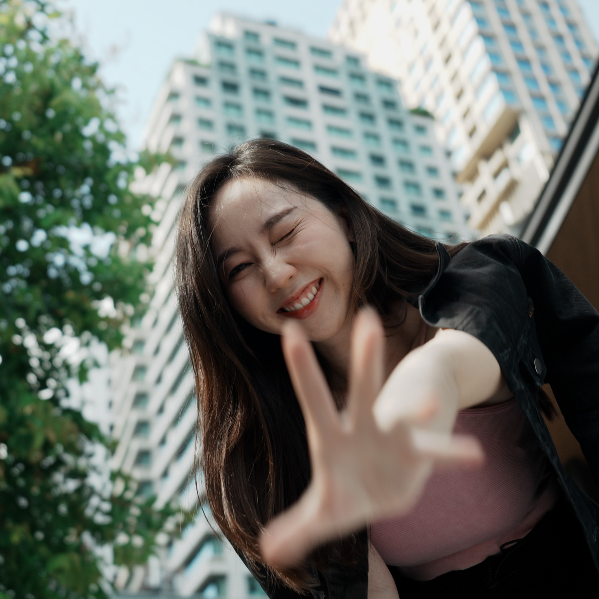 Girl winking with a smile and hand reaching out to the camera captured from a lower angle