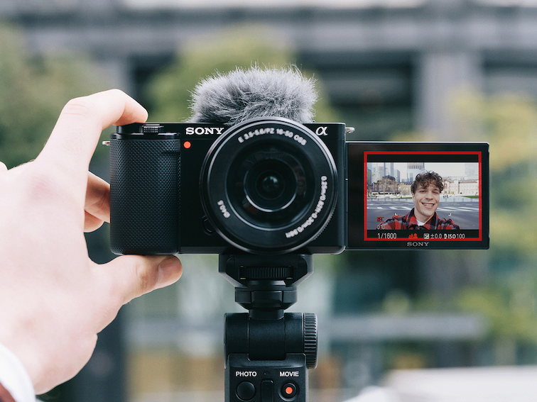 Man holding up a camera and smiling into the front-facing monitor