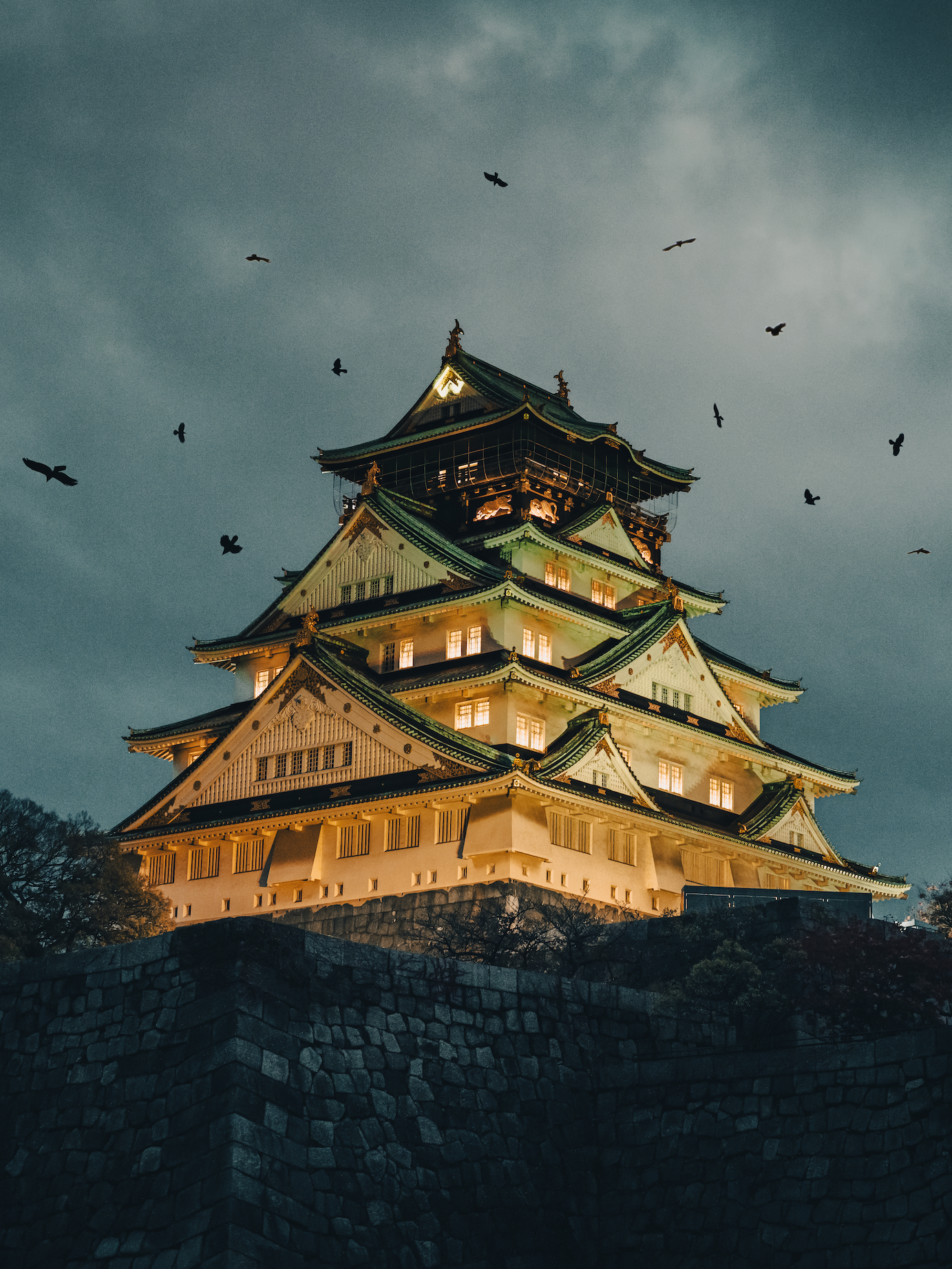 A brightly lit Osaka Castle at nightfall with birds flying around it